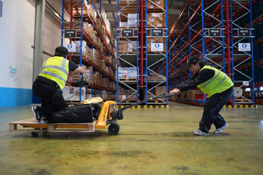 two-workers-moving-pallet-with-hand-truck-in-warehouse-52dt0ywnjyo